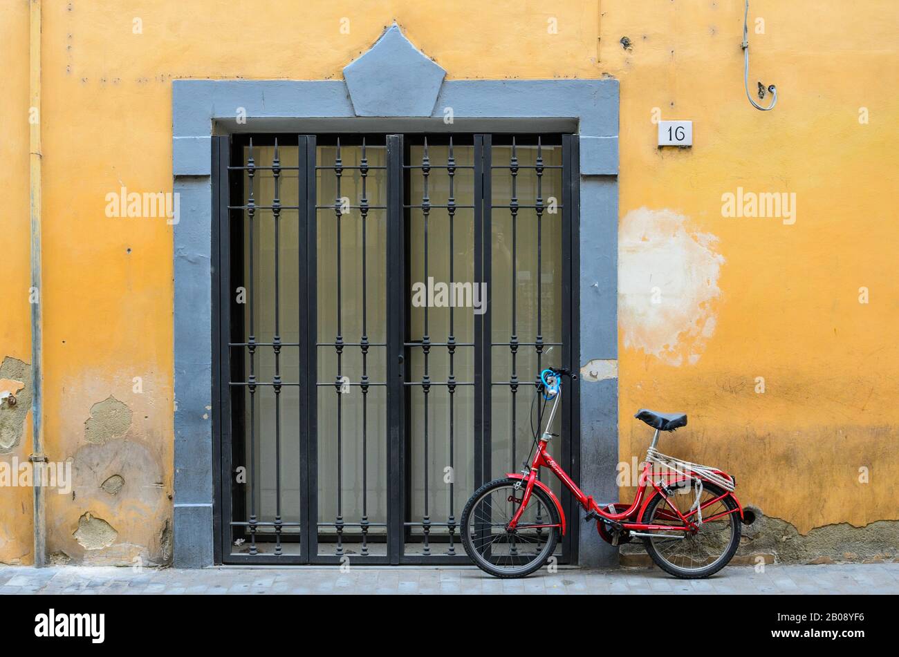 Porte d'un bâtiment peint en jaune, avec un vieux vélo rouge soutenu contre lui. Pise, Italie. Banque D'Images