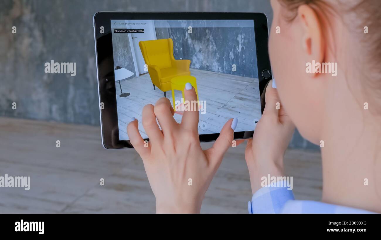 Femme utilisant une tablette avec application de réalité augmentée et plaçant des meubles en relief dans la pièce Banque D'Images