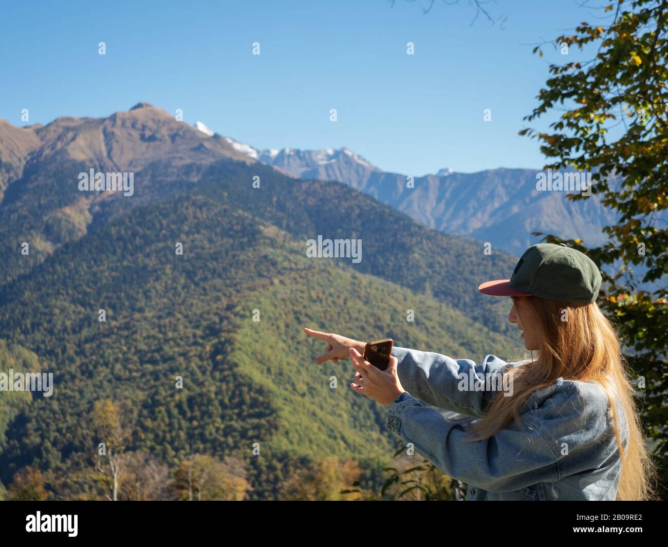 Une fille aux cheveux longs tient un téléphone dans sa main et pointe le doigt sur les pics de montagne Banque D'Images