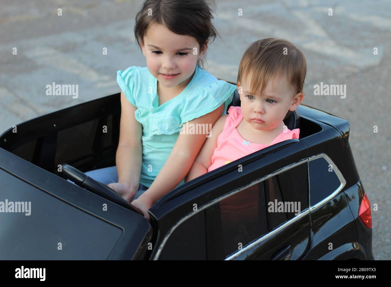 Deux superbes filles vont dans une grande voiture jouet sur l'asphalte de la rue de la ville. Conduite en plein air dans une attraction estivale pour les enfants Banque D'Images