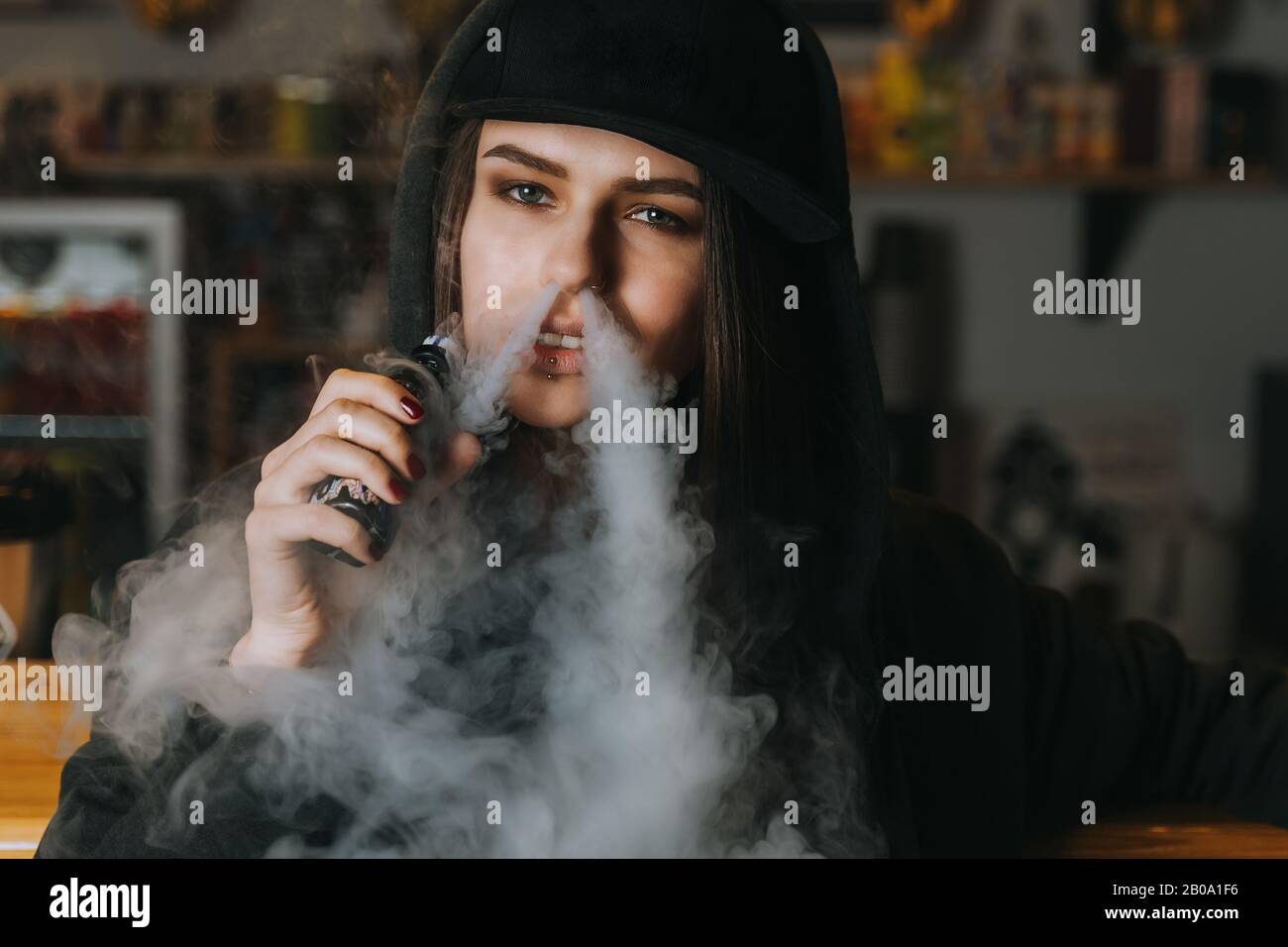 Une jeune jolie femme dans la calotte fume une cigarette électronique à la  boutique de vaque. Style hip-hop. Gros Plan Photo Stock - Alamy