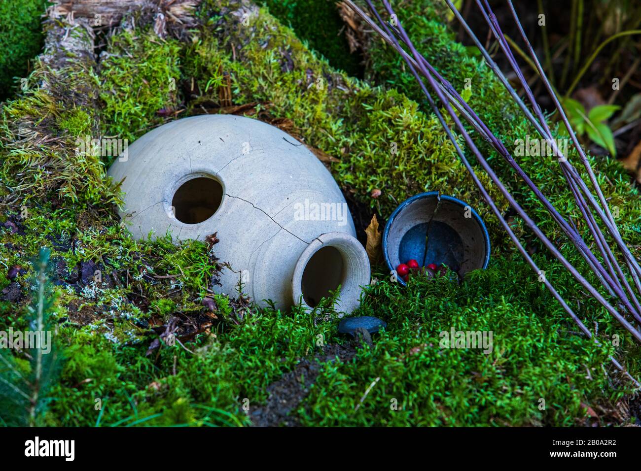 Gros plan d'une maison de fées magique dans une forêt, avec une bosse couverte de mousse, une urne de pierre renversée, des baies rouges, des brindilles. Copier l'espace vers la droite Banque D'Images