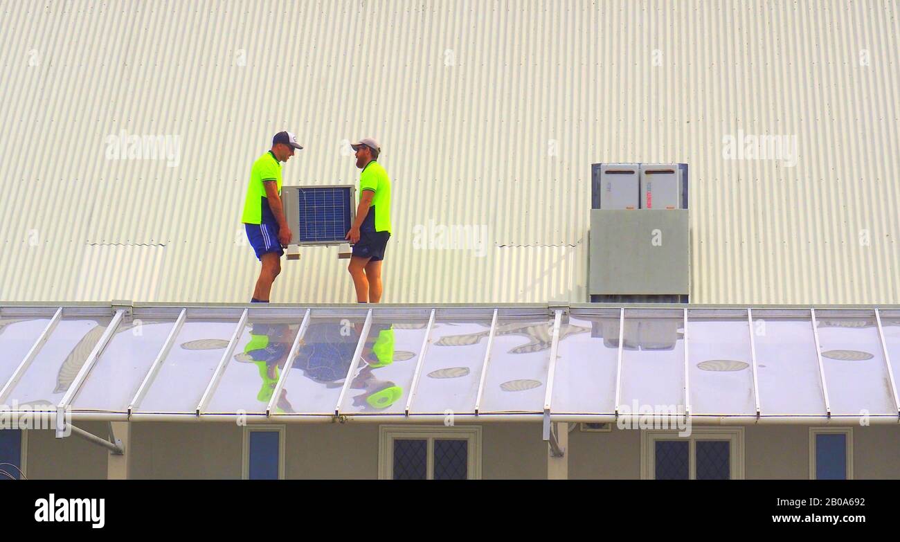 Deux travailleurs sont porteurs d'une nouvelle unité de climatisation en haut d'un bâtiment Banque D'Images