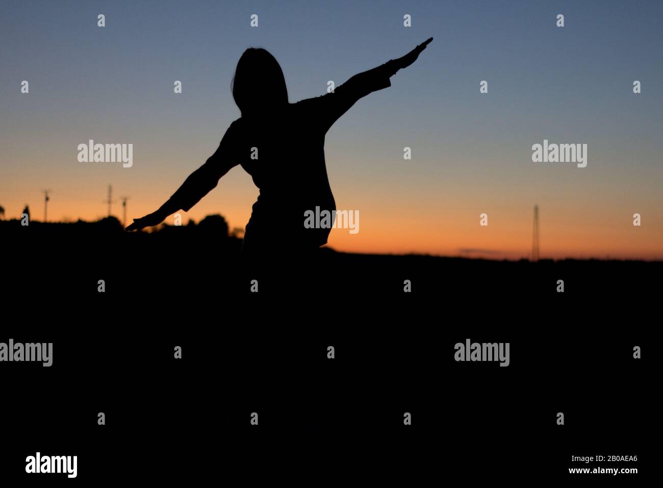 Une femme enceinte avec son bras relevé est silhouettée contre un soleil coloré Banque D'Images
