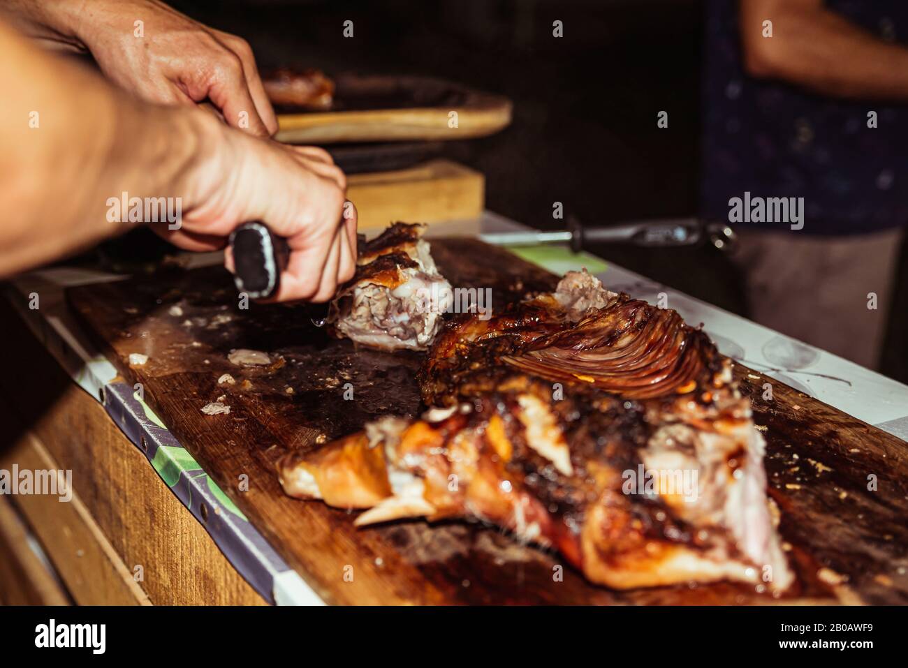 Le chef coupe le porc grillé dans des steaks avec couteau. Cochon de succion traditionnel cuit sur le gril à charbon. Le petit cochon est grillé dans son ensemble sur un o Banque D'Images
