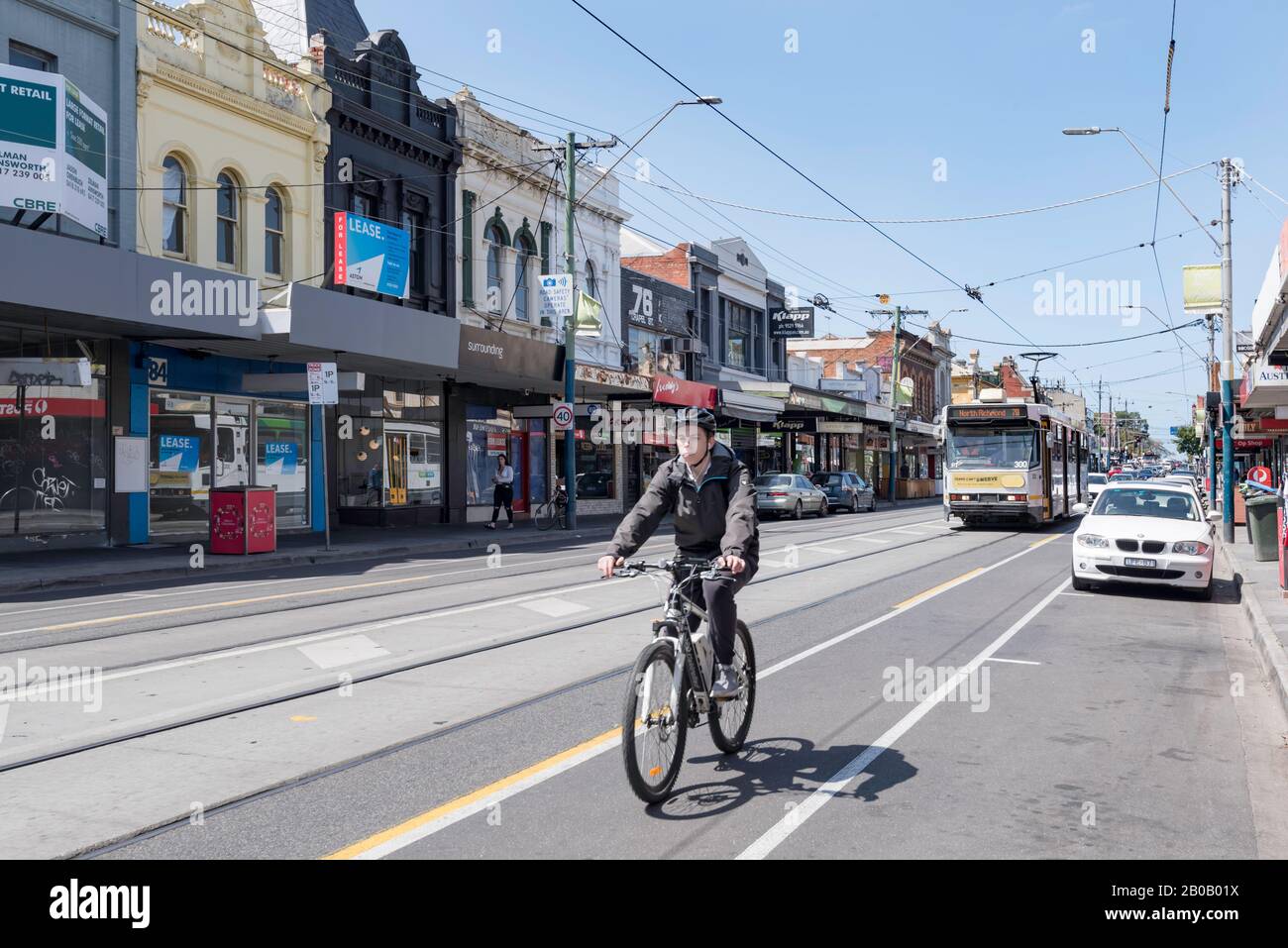 Un cycliste qui monte son vélo sur une piste cyclable dédiée sur Chapel Street, Windsor, Melbourne, Australie avec un tram qui suit sur la même route Banque D'Images