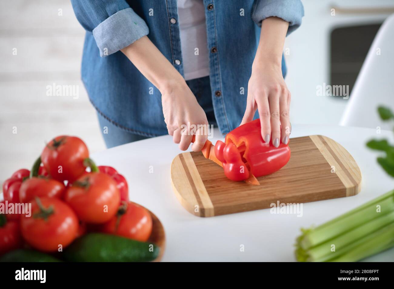 Mains féminines avec couteau coupant une tranche de poivron rouge. Banque D'Images
