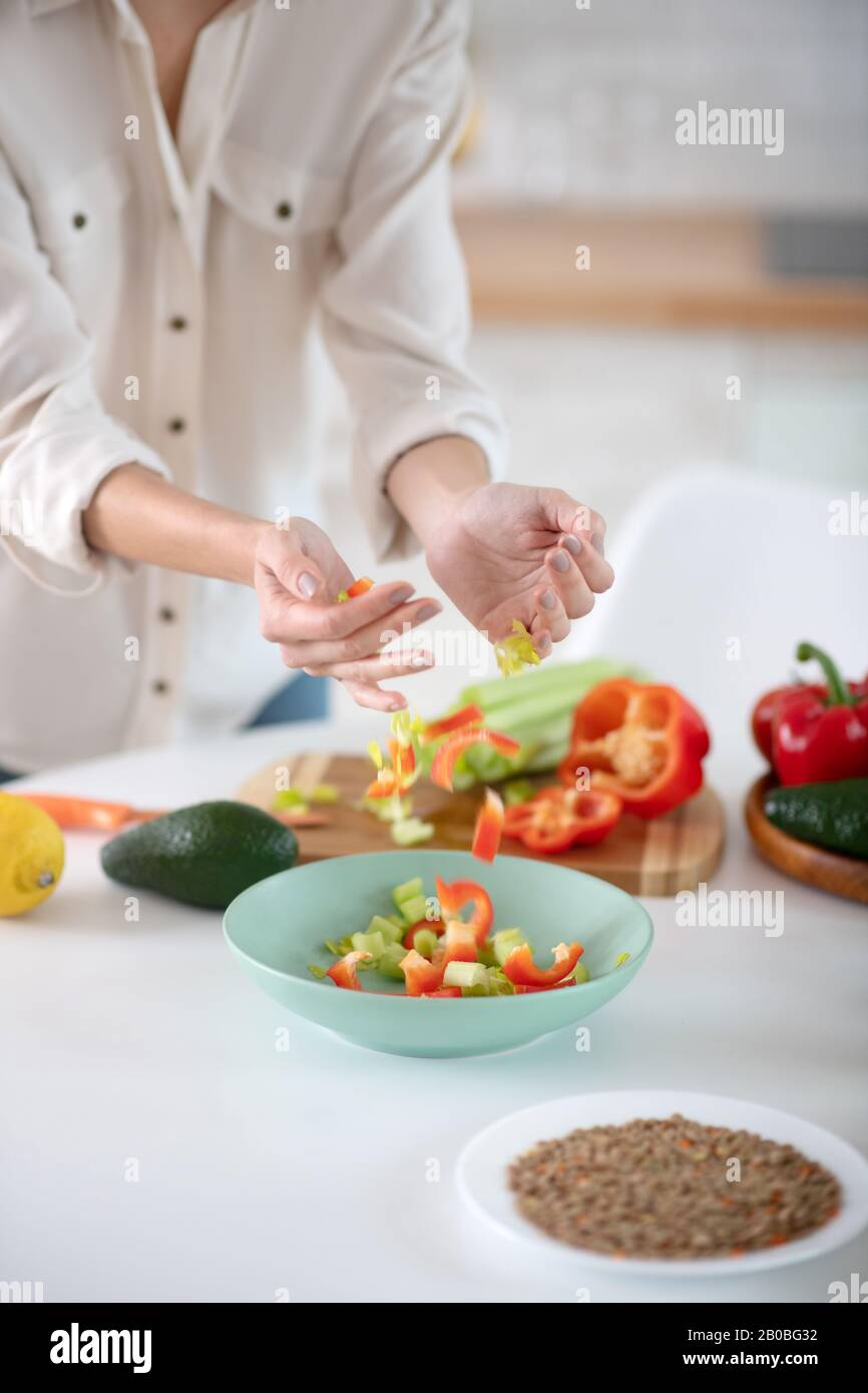 Mains féminines versant des légumes déchiquetés dans une assiette. Banque D'Images