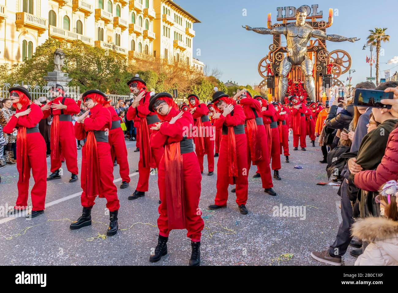 Des personnages masqués dansant dans la rue avec le flotteur allégorique "Idol" en arrière-plan, Carnaval de Viareggio, Italie Banque D'Images