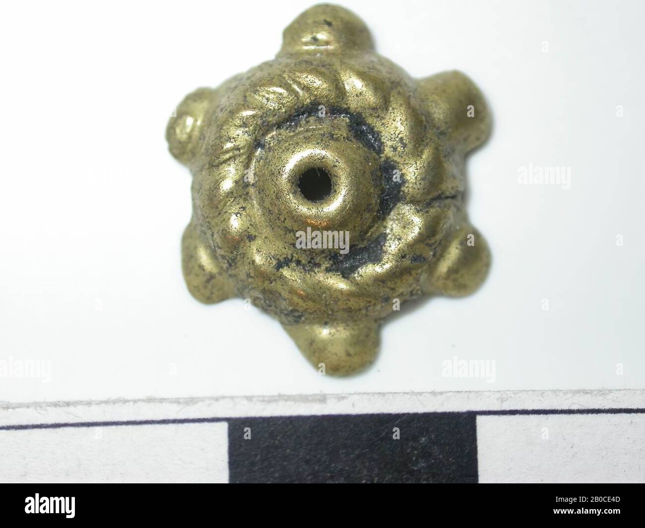 Forme circulaire, or (alliage de cuivre). Forme circulaire avec une forme convexe au milieu avec un trou. Autour, il s'agit d'une couronne avec des rayures diagonales. Il y a 6 saillies. Le dos est creux. fixation à 1 broche. Code PIN manquant. Le diamètre du trou est de 0,1 cm, course de la courroie, métal, plomb Banque D'Images