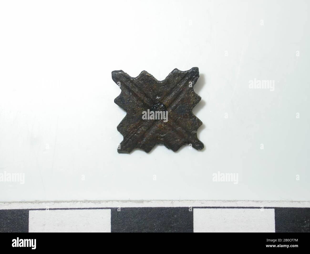 Forme carrée, or (alliage de cuivre). Forme carrée avec bords dentelés. Diagonale au-dessus du milieu. Une broche a été perforée par le milieu. L'arrière est plat. fixation à 1 broche. La goupille est carrée. La longueur est de 0,2 cm. Épaisseur : 0,2 cm, course du tapis, métal, alliage de cuivre, H : 1,1 cm, W : 1,1 cm, D : 0,1 cm, fin du XIVe siècle 1350-1400, Pays-Bas, Zélande, Hulst, Verdronken Land Banque D'Images