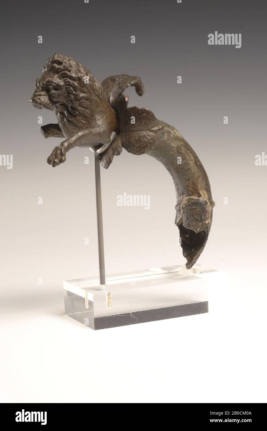Oreille en bronze d'une verseuse, sous forme de proto d'un lion. La poignée  creuse a été décomposée au fond et a été partiellement remplie de plâtre.  La poignée se termine en quatre