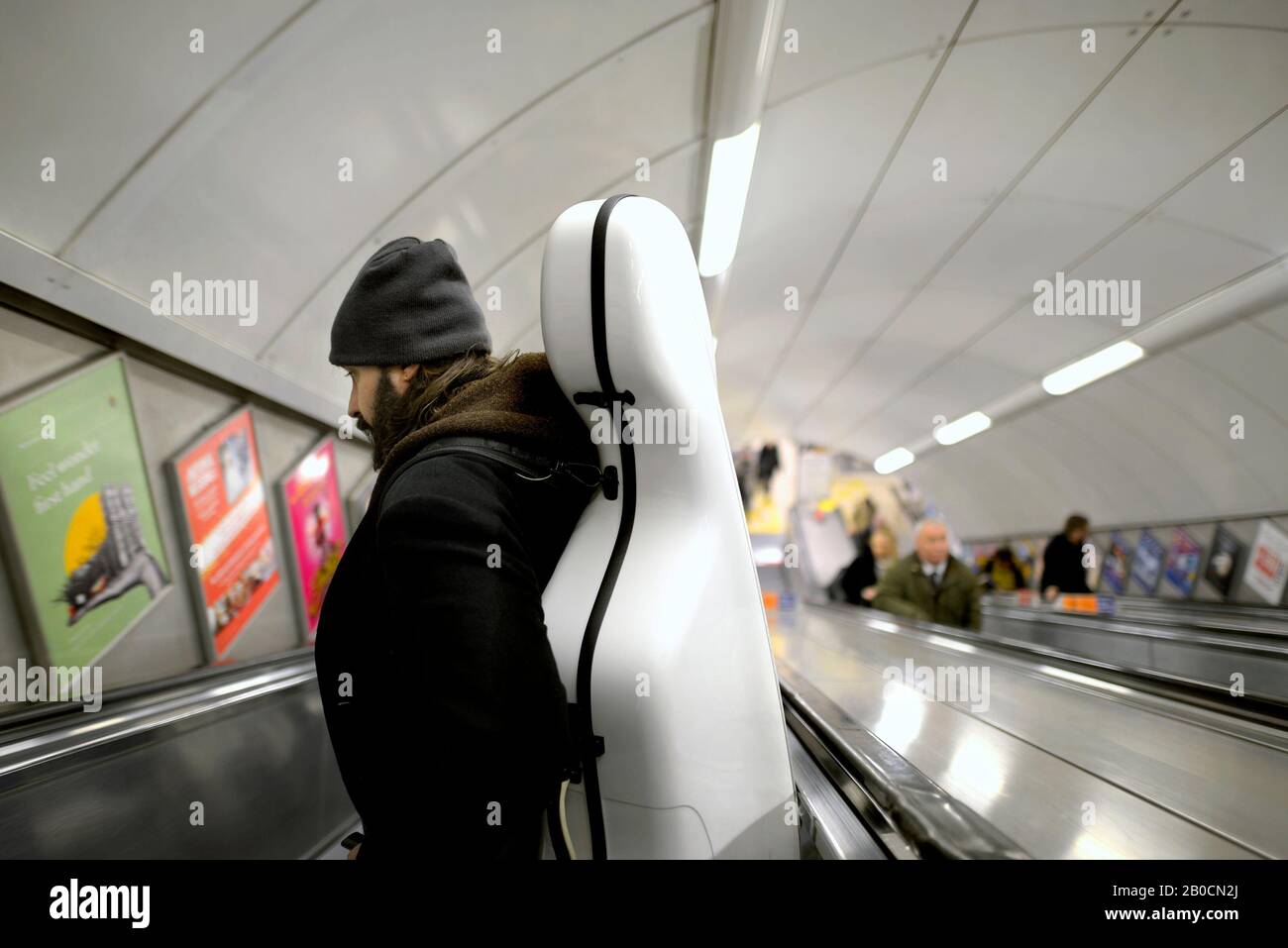 Londres, Angleterre, Royaume-Uni. Homme transportant un violoncelle vers le bas d'un escalator dans une station de métro Banque D'Images