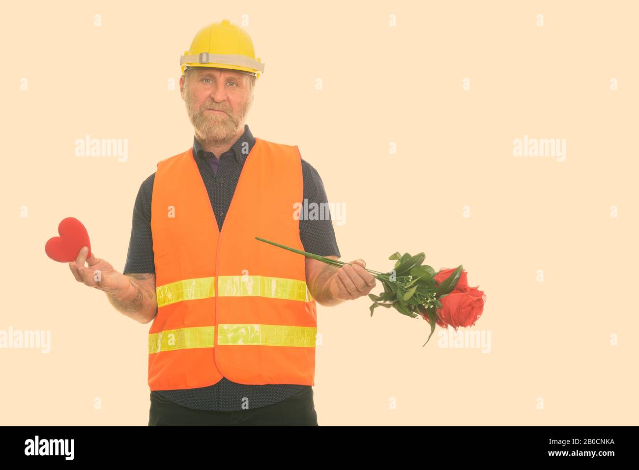 Triste homme à maturité barbu travailleur de la construction tenant le cœur rouge et les roses Banque D'Images