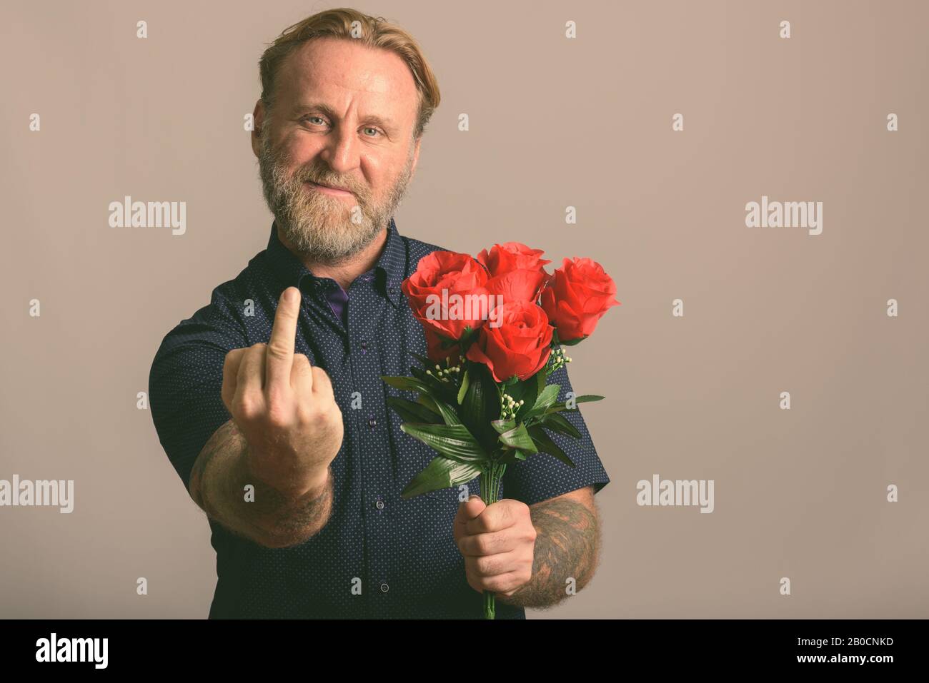 Homme à maturité heureux tenant des roses rouges tout en montrant le doigt central Banque D'Images