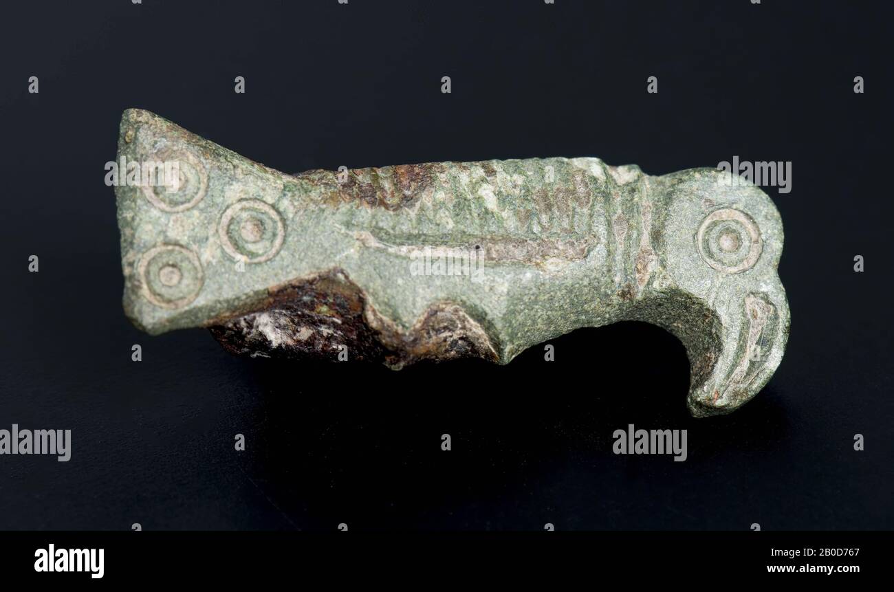 Fibula d'oiseau en bronze, en forme d'oiseau de proie (oiseau avec grand bec courbé et queue triangulaire), décoré avec des décorations à encoches, oeil (cercle de points), lignes transversales sur le cou, sur la longueur du corps, une bande dont les bandes croisées gauche et droite ressemblent à des griffes. Dans la queue, quatre cercles de point dans un triangle, à l'arrière de matière noire caillée, mais une ceinture de jeu peut être vue. Spirale avec aiguille., Fibula, fibula oiseau, métal, bronze, hauteur 2,7 cm, largeur 1,0 cm, épaisseur 0,7 cm., Vme 470-530, Pays-Bas, Gueldre, Beuningen, Ewijk, Koningstraat Banque D'Images