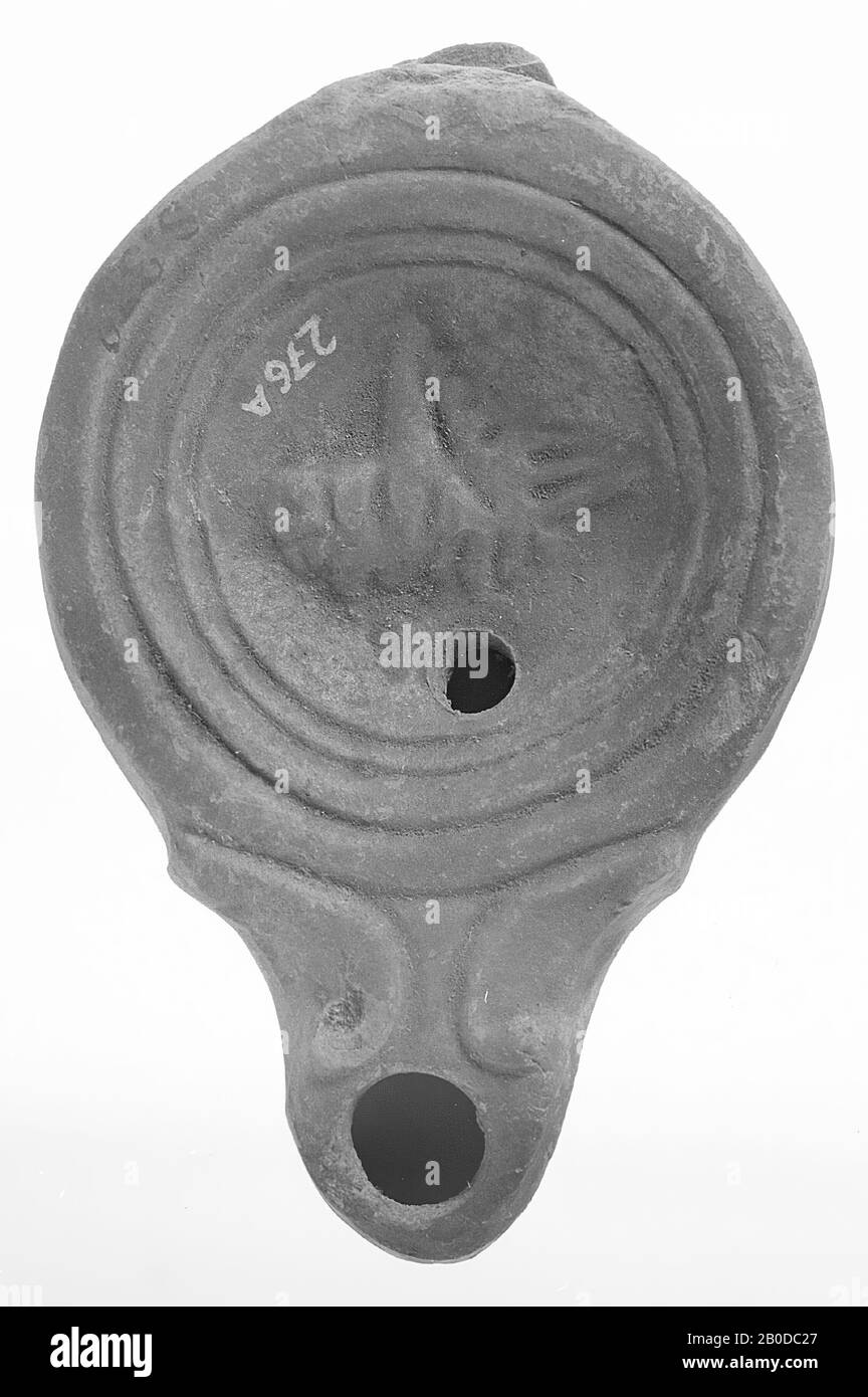 Une lampe à huile imbriquée en rouge avec un corps rond sur un socle encastré. Le miroir concave est entouré de cercles concentriques encastrés et est décoré avec une image relief d'une sauterelle. Le bec court et large avec un grand trou de feu est décoré de volutes et rond fermé. Le petit trou de remplissage est situé sous la figure., lampe à huile, faïence, terre cuite, 3.5 x 10.2 x 6.2 cm, 1ère et 2ème siècle AD. 1-200, Asie Banque D'Images