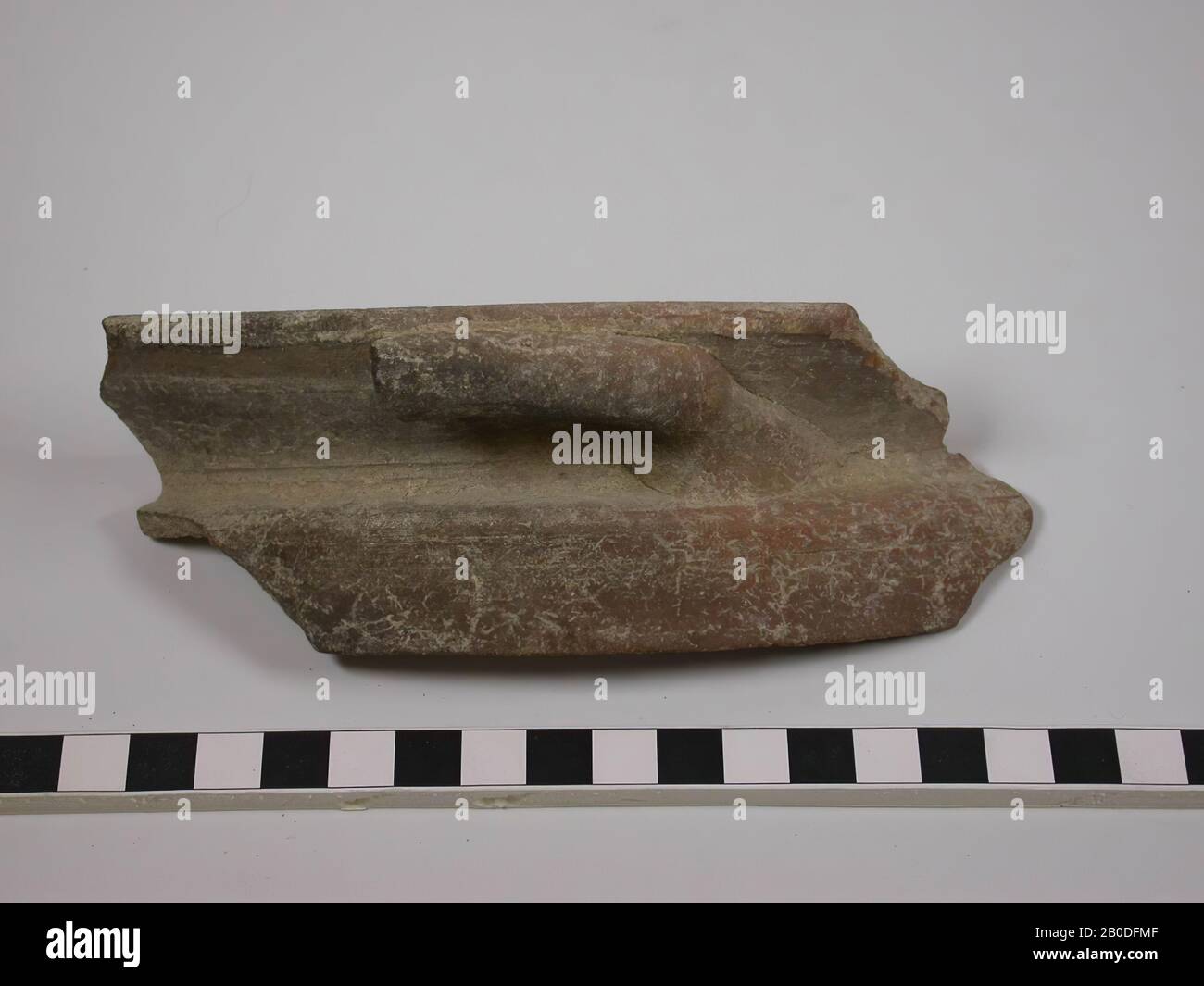 Fragment du bord et poignée d'un pot de cuisson. Lorsque la paroi se fusionne dans le bord, un bord-cache est d'abord dessiné horizontalement vers l'intérieur, après quoi un angle aigu garantit un bord de projection éloigné vers l'extérieur. Une poignée est fixée à la partie saillante du bord. La poignée est fixée sur le bord dans son intégralité et a été démolie à mi-chemin. La couleur est rouge Banque D'Images