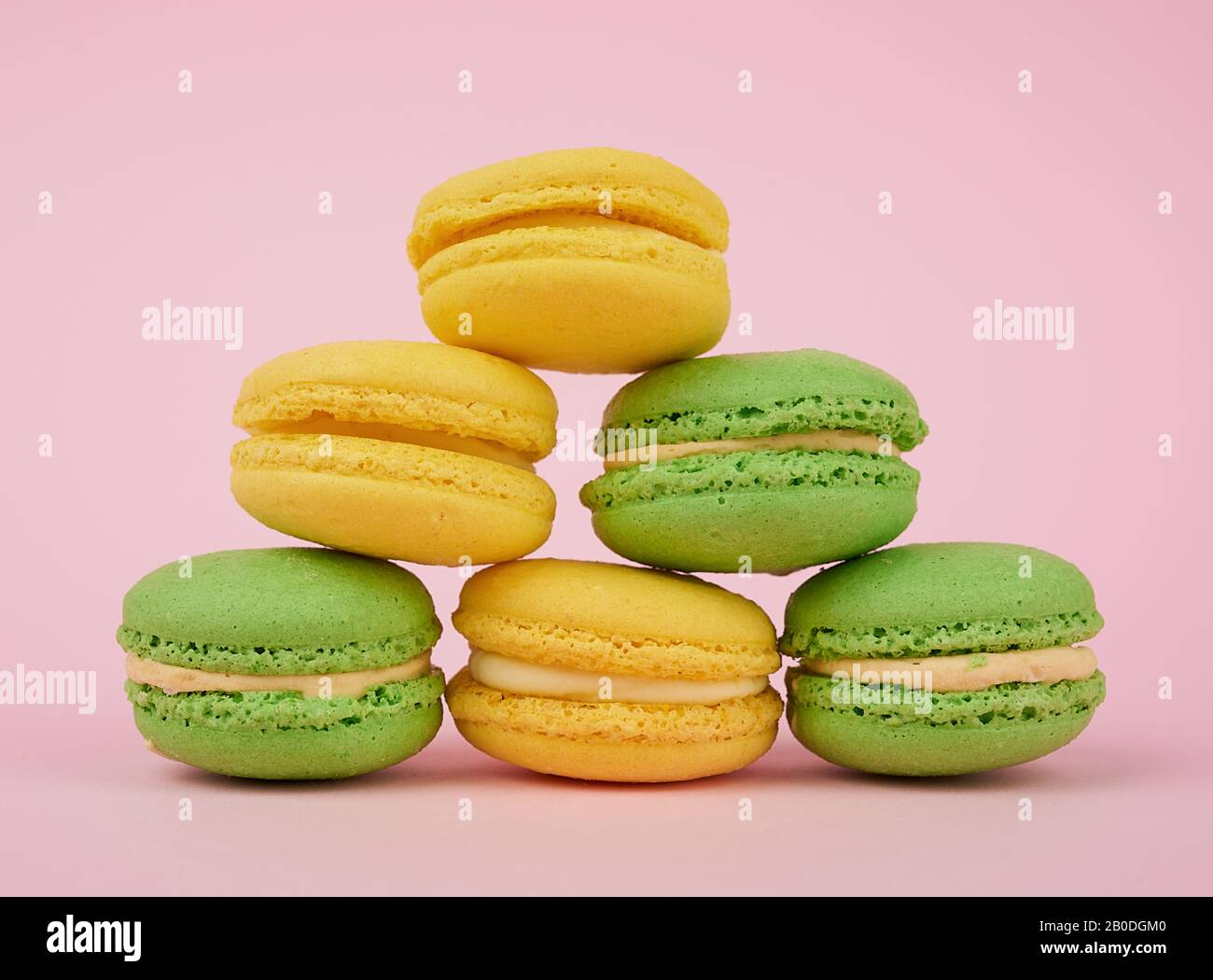 une pile de macarons de gâteaux de farine d'amande ronde jaune et verte avec de la crème sur un fond rose, un délicieux gâteau Banque D'Images