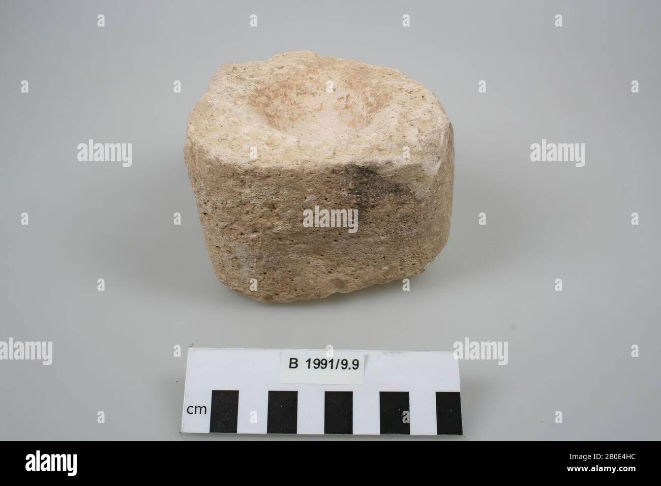 Mortier (ou tourniquet de porte?) De calcaire blanc. Haut et triangulaire en coupe transversale avec coins arrondis. Le haut et le bas sont plats et ont une surface rugueuse. Au milieu du haut se trouve un creux rond. La cavité a une surface rose-blanc avec de la terre brune et de fines rainures concentriques et des crêtes. Les côtés ont une surface plane avec un dépôt gris foncé ou de la saleté et des dépôts blancs. Certains plis des bords sont manquants. Le calcaire contient de petits trous et des parties chatoyantes., pierre à affûter, élément de construction, pierre, calcaire, L 10,8 cm, W 9,8 cm, H 7,3 cm, Jordanie Banque D'Images
