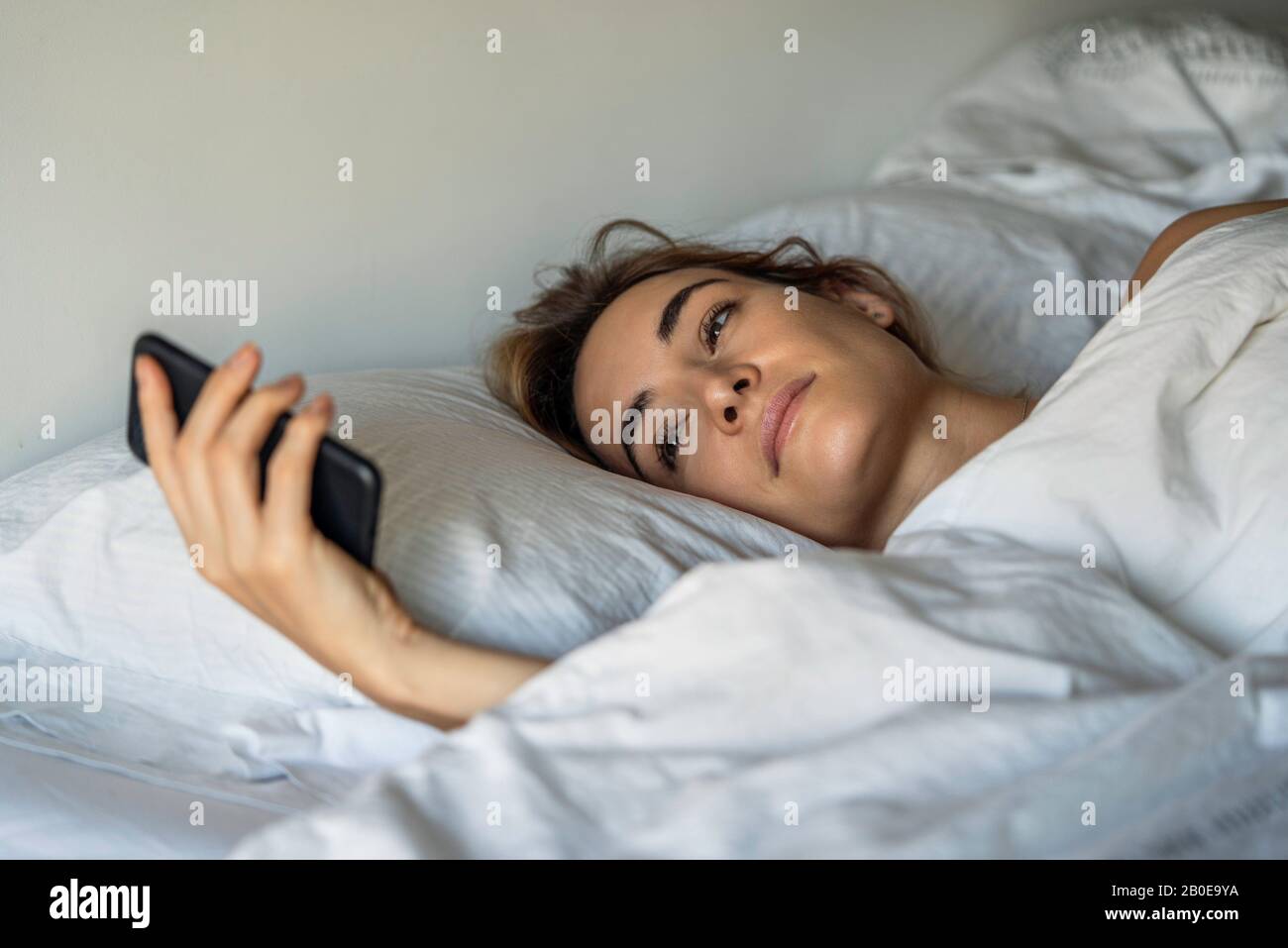 Jeune femme regardant un smartphone sur le lit Banque D'Images