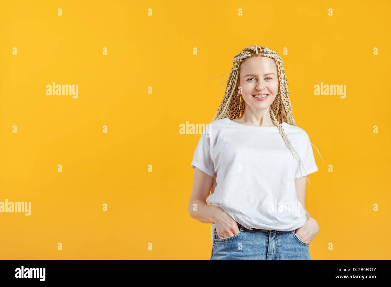 Hipster mode fille souriante avec kanekalon sur fond jaune. Jeune femme  sympa et positive avec un t-shirt blanc souriant et bretelles Photo Stock -  Alamy