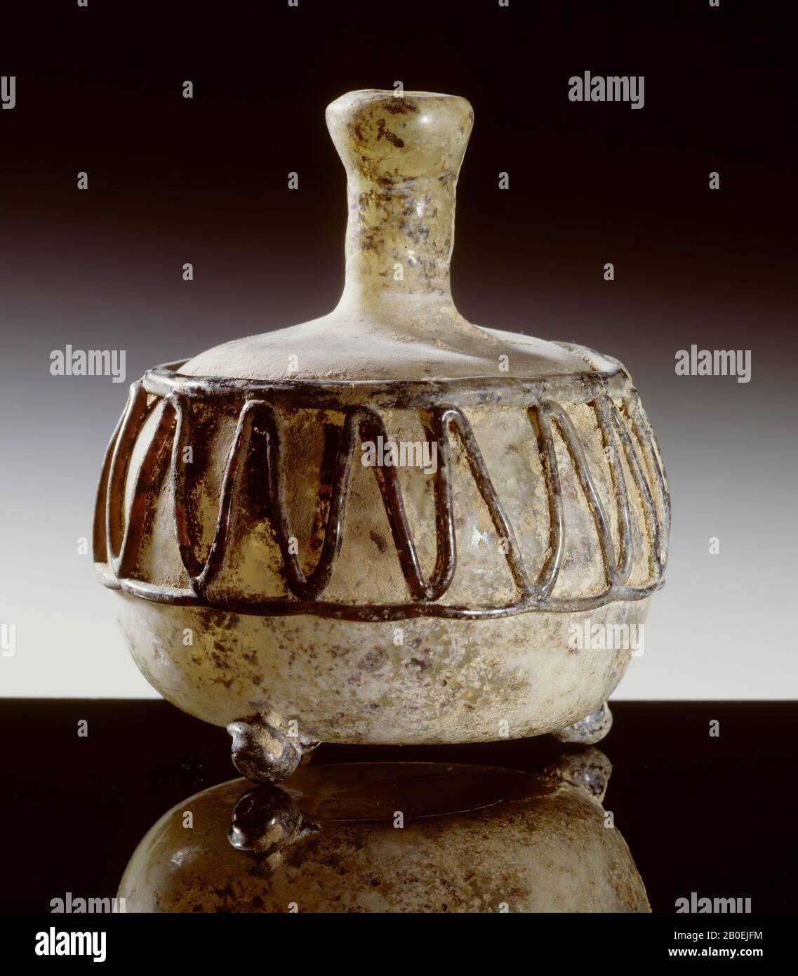 Bouteille de verre vert pâle, à col court, sur trois pieds sphériques. Le corps cylindrique a deux lignes horizontales, avec un fil vert entre elles. Les fils de décharge et les jambes sont vert foncé Banque D'Images