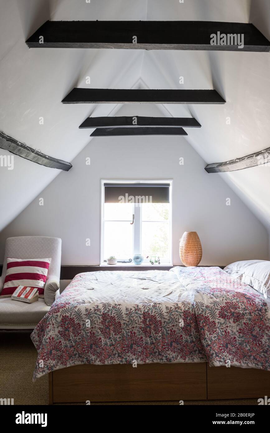 Chambre mansardée meublée simplement avec fauteuil couvert de lin français du XIXe siècle à côté du lit. Couette d'Oka. Banque D'Images