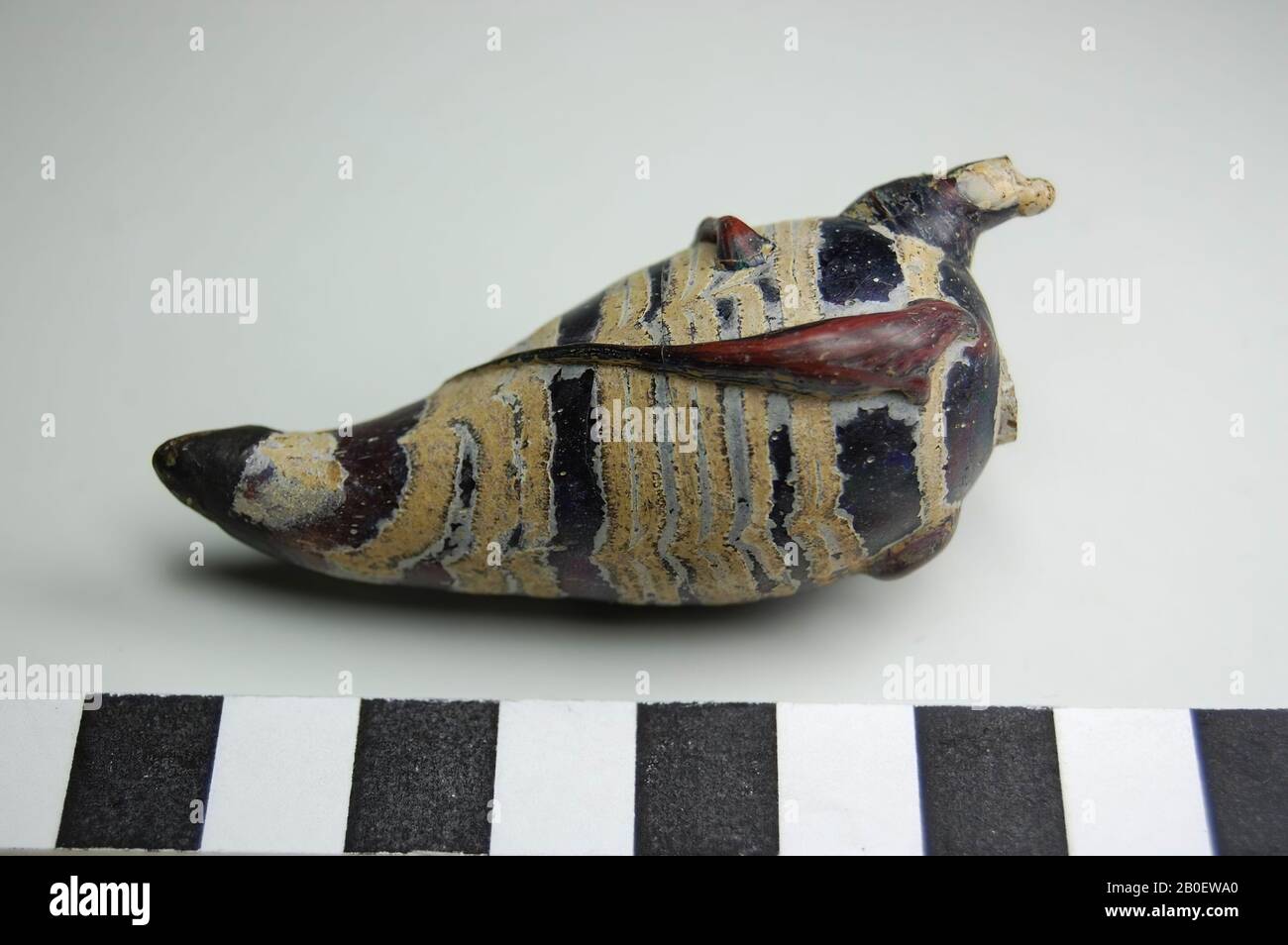 oiseau, oiseau en verre violet foncé transparent avec bandes blanches opaques. Probablement utilisé comme une amulette ou une bouteille cosmétique. L'oiseau a un corps allongé avec une tasse relativement petite. Les jambes et les ailes sont suggérées au moyen de fils de verre épais et Banque D'Images