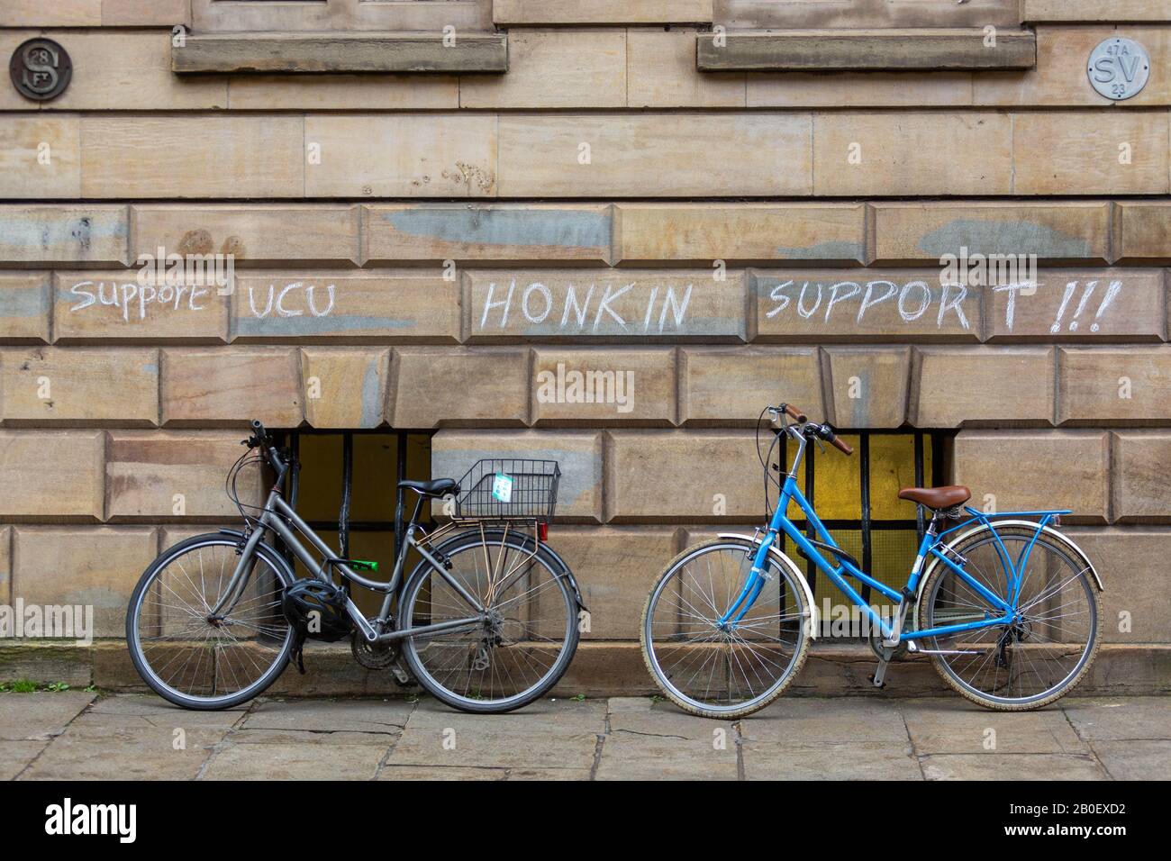 Cambridge, Royaume-Uni. 20 février 2020. Deux vélos sont garés contre un mur de pierre près de la bibliothèque Hadden, Cambridge, où le graffiti à la craie indique « support UCU SUPPORT HONKIN ! ! ! » en caractères gras et expressifs. Le message témoigne de la solidarité avec la grève de l'Union universitaire et collégiale (UCU), reflétant le soutien de la base pour le personnel académique et ses revendications pour des salaires et des conditions de travail équitables. Penelope Barritt/Alamy Live News Banque D'Images