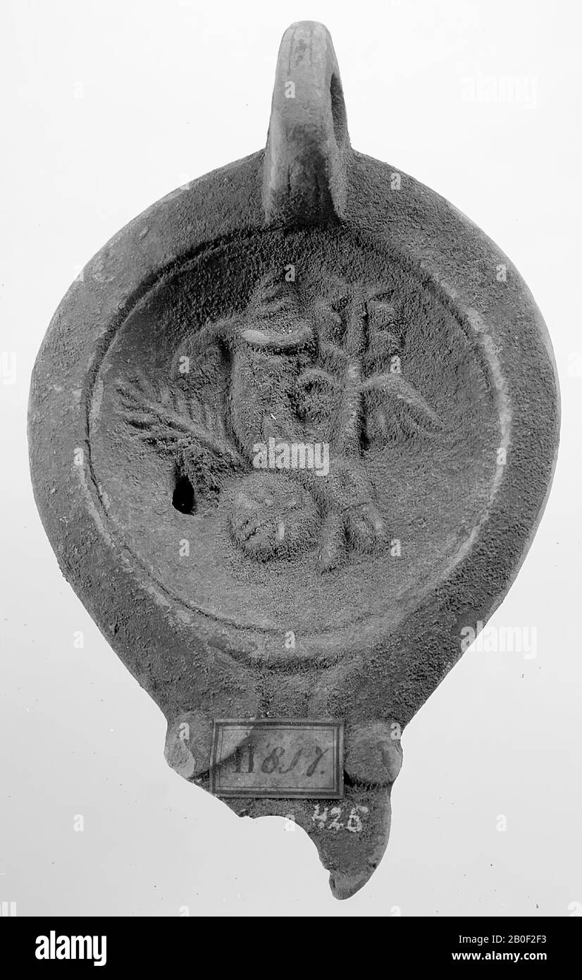 Une lampe imbriquée en rouge avec un corps ovale sur une base ronde encastrée. Le miroir concave est entouré d'un cercle encastré et décoré avec un relief de palmier, une cornucopie et un personnel Hermès. Le petit bec large était décoré de volutes. L'oreille fixée verticalement est décorée avec des encoches. Le petit trou de remplissage se trouve à gauche de l'image. Marque: L.M.C. (?), lampe à huile, faïence, terre cuite, 4.8 x 12.5 x 7.9 cm, 1ère et 2ème siècle après J.-C. 1-200 AD, Tunisie Banque D'Images