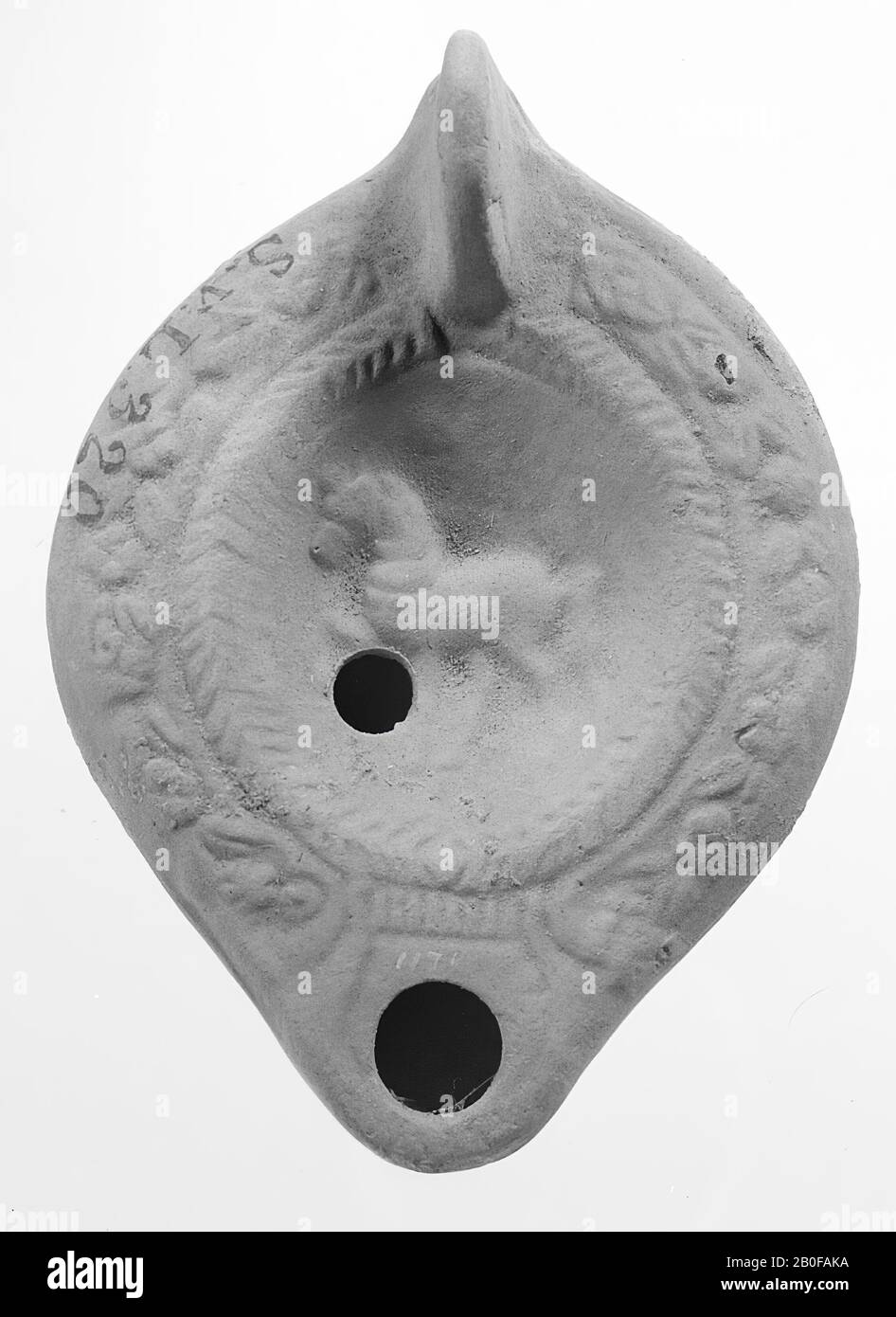 Une lampe de terre rouge clair avec un corps de forme ovale sur une base ronde. Le miroir rond est entouré d'une branche de palmiers et décoré avec un cheval debout entouré de feuilles avec un petit trou de remplissage. L'épaule est décorée avec des tendrils. Le bec court et arrondi est doté d'un grand trou d'incendie. La poignée fixée verticalement s'étend jusqu'au fond du socle., lampe à huile, faïence, terre cuite, 3,9 x 9,9 x 7,1 cm, 4ème, 5ème et 6ème siècle après J.-C. 300-600, Turquie Banque D'Images