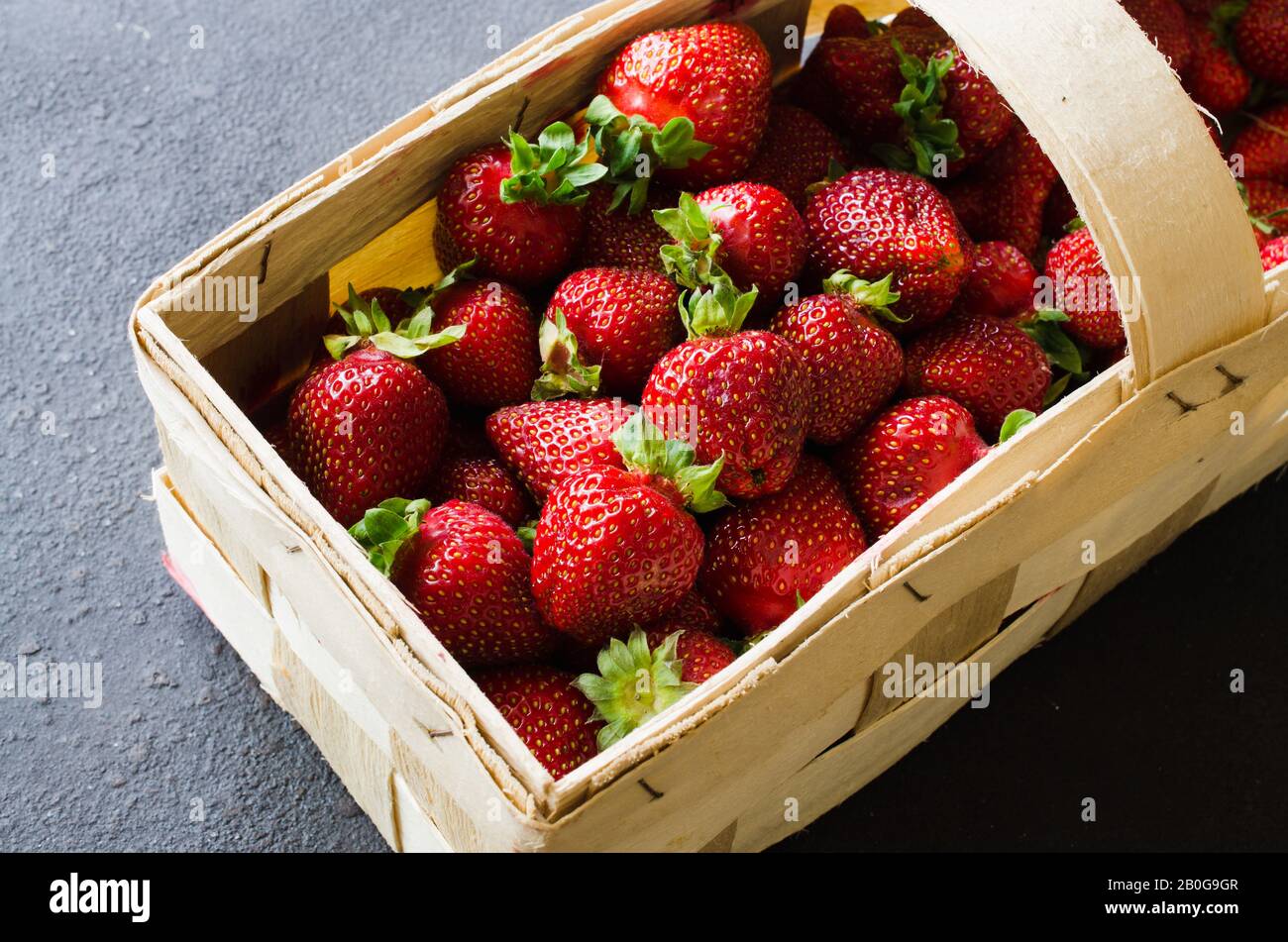 Les fraises mûres fraîches dans un panier en bois sur un fond sombre. Petits fruits juteux organique. Vue d'en haut. Copie de l'espace pour votre texte. Banque D'Images
