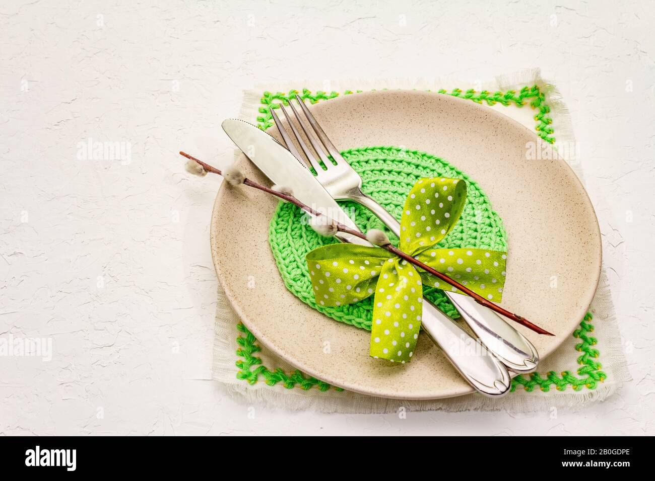 Réglage de la table de Pâques sur fond de putty blanc texturé. Modèle de carte vacances de printemps. Couverts, serviette brodée, noeud, sceaux saules, espace de copie Banque D'Images