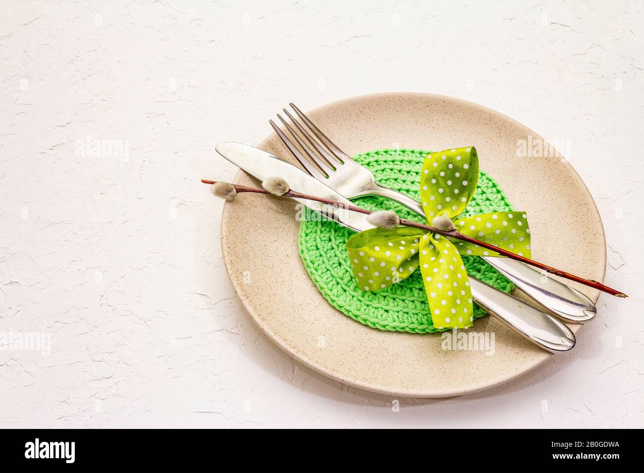 Réglage de la table de Pâques sur fond de putty blanc texturé. Modèle de carte vacances de printemps. Couverts, serviette tricotée, noeud, sceaux saules, espace de copie Banque D'Images