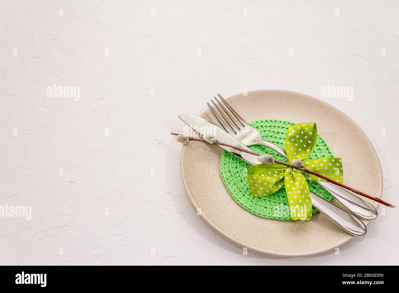 Réglage de la table de Pâques sur fond de putty blanc texturé. Modèle de carte vacances de printemps. Couverts, serviette tricotée, noeud, sceaux saules, espace de copie Banque D'Images