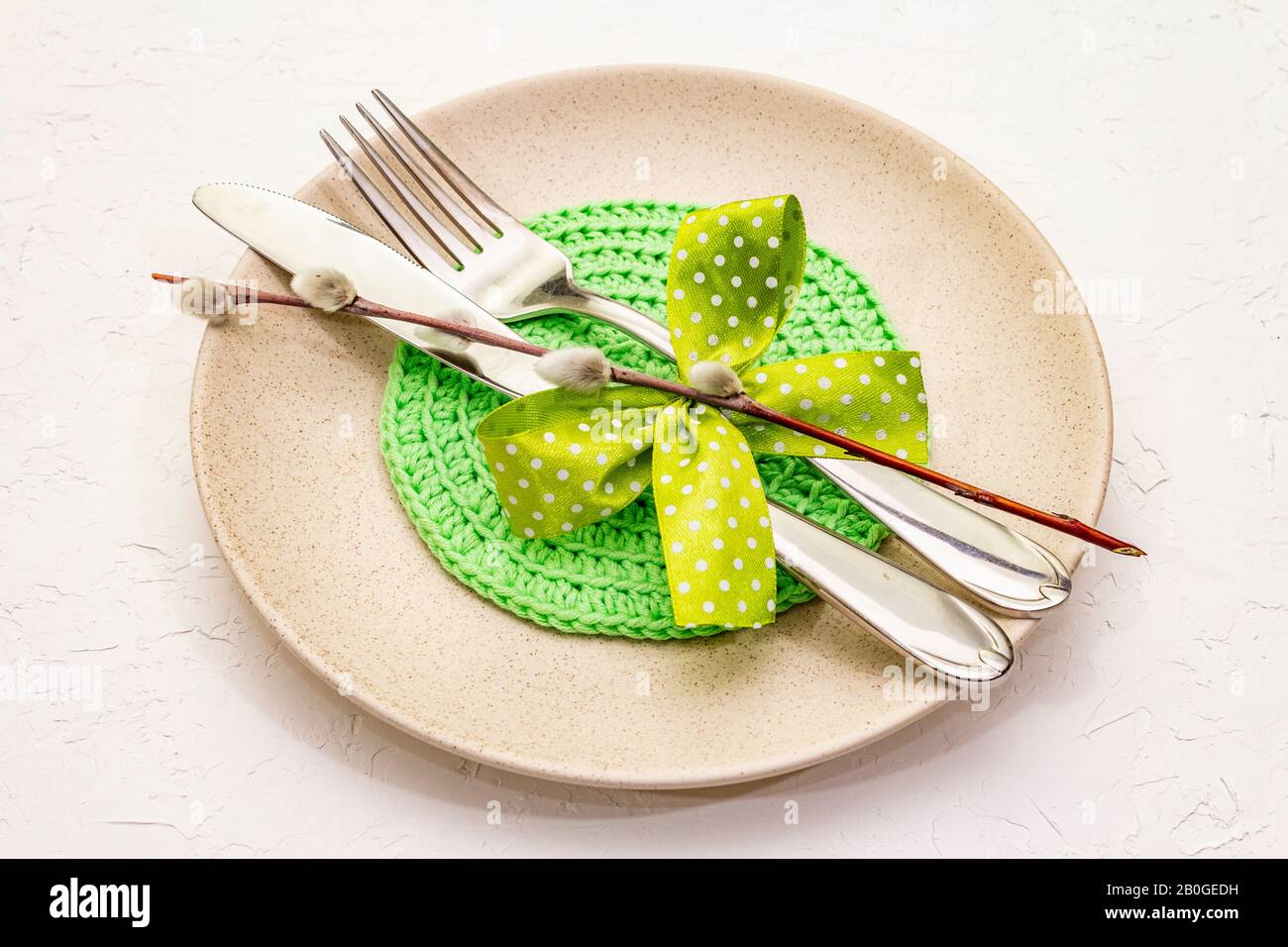 Réglage de la table de Pâques sur fond de putty blanc texturé. Modèle de carte vacances de printemps. Couverts, serviette tricotée, noeud, joints de saule, gros plan Banque D'Images