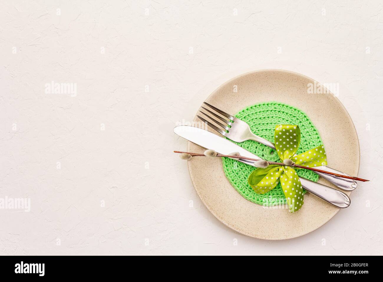 Réglage de la table de Pâques sur fond de putty blanc texturé. Modèle de carte vacances de printemps. Couverts, serviette tricotée, noeud, sceaux saules, espace de copie, vie supérieure Banque D'Images