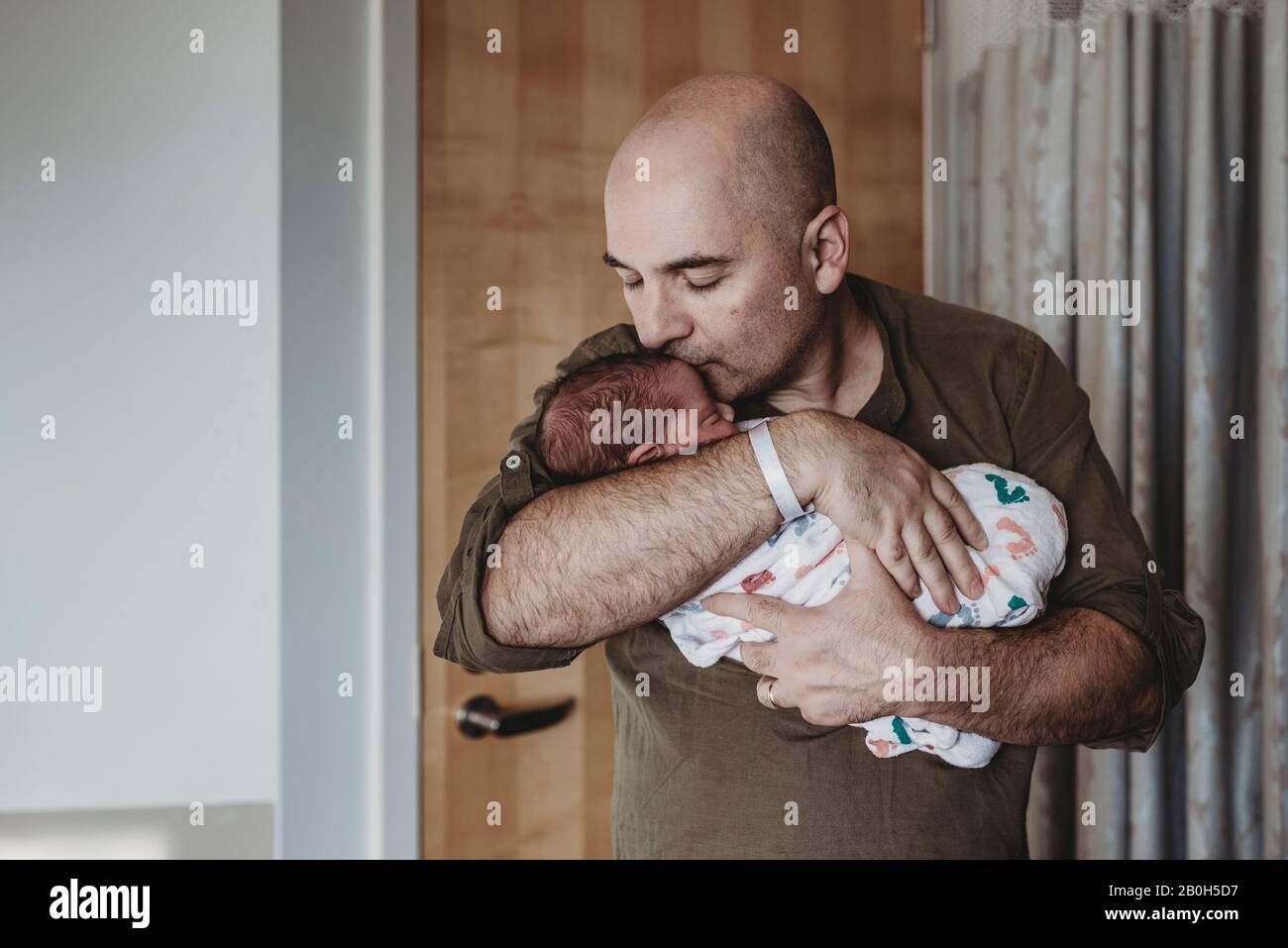 Un père heureux embrasse un nouveau-né enveloppé de couvertures à l'hôpital Banque D'Images