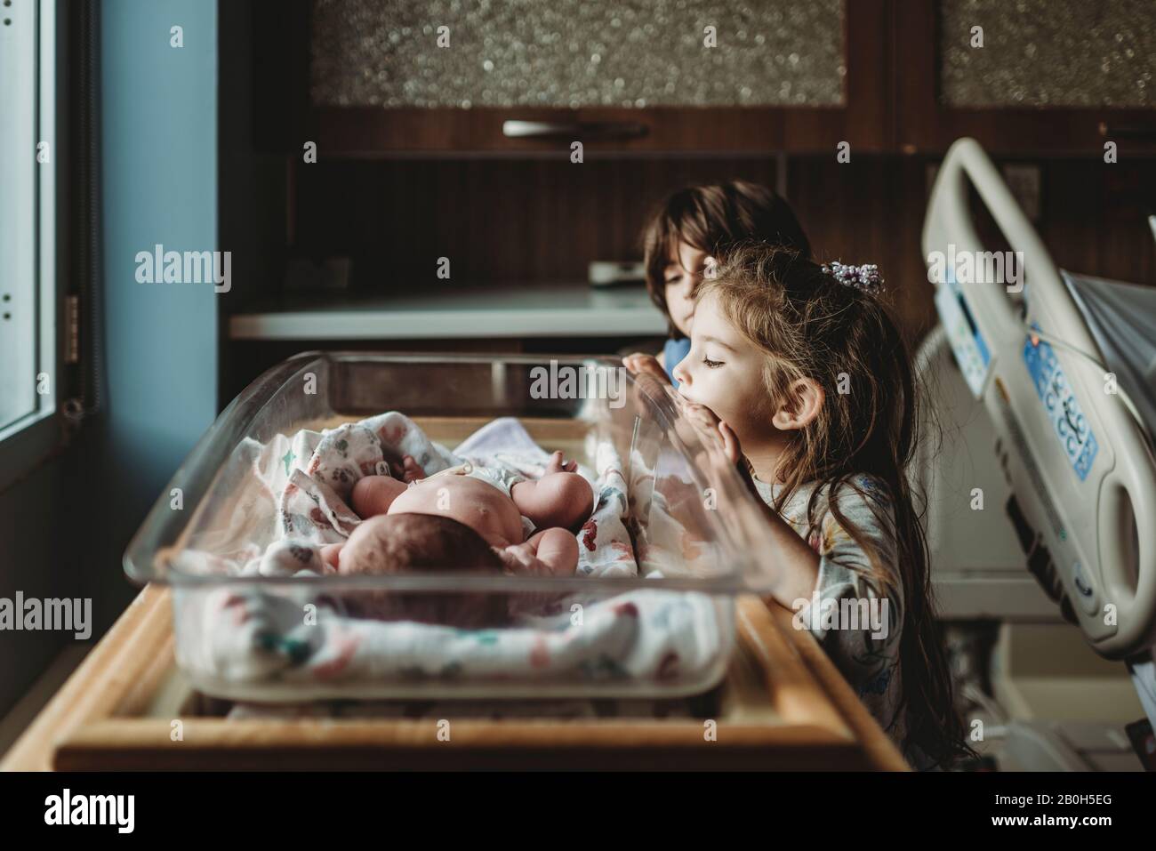 Sœurs regardant le frère nouveau-né dans un berceau d'hôpital Banque D'Images