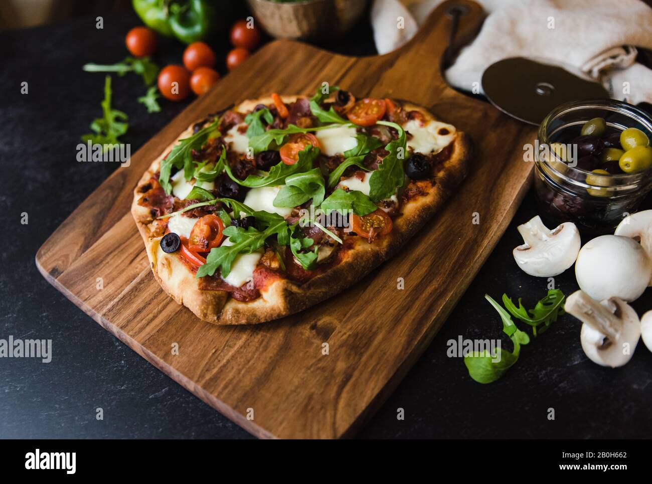 Gros plan de pizza faite à la main sur un panneau de bois avec des ingrédients autour. Banque D'Images