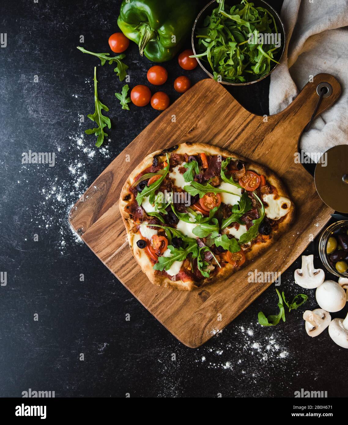 Vue de dessus de pizza faite à la main sur un panneau de bois avec des ingrédients autour. Banque D'Images