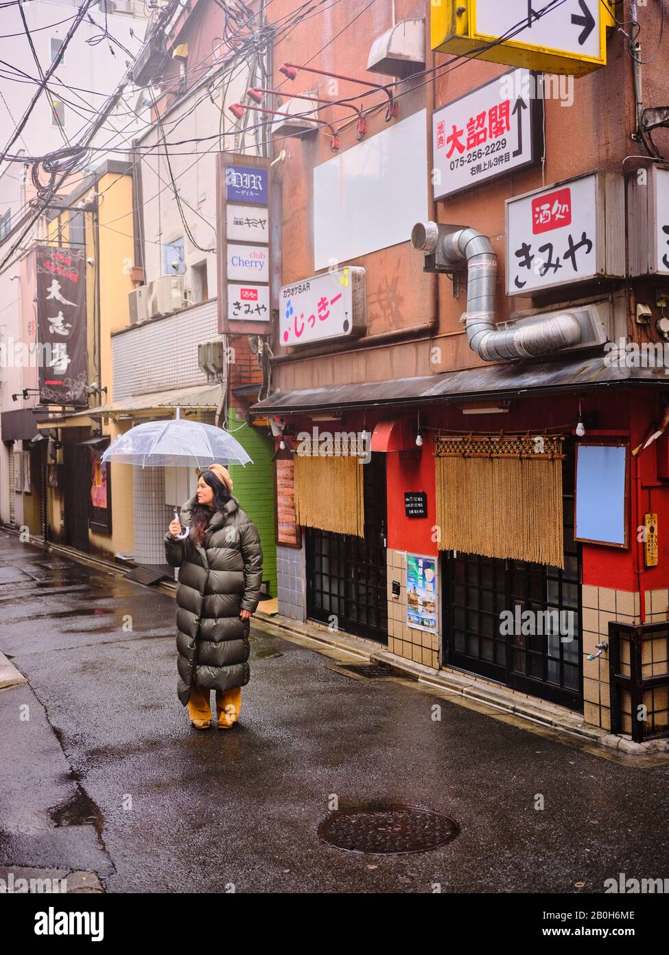 Femme dans une longue veste de pluie tient avec parapluie dans une allée Kyoto Japon Banque D'Images