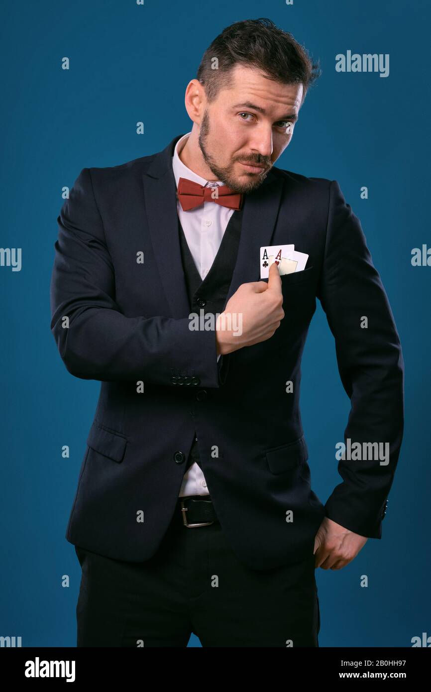 Homme en costume classique noir et noeud-cravate rouge montrant deux cartes  de jeu tout en posant sur fond bleu studio. Jeu, poker, casino. Gros plan  Photo Stock - Alamy
