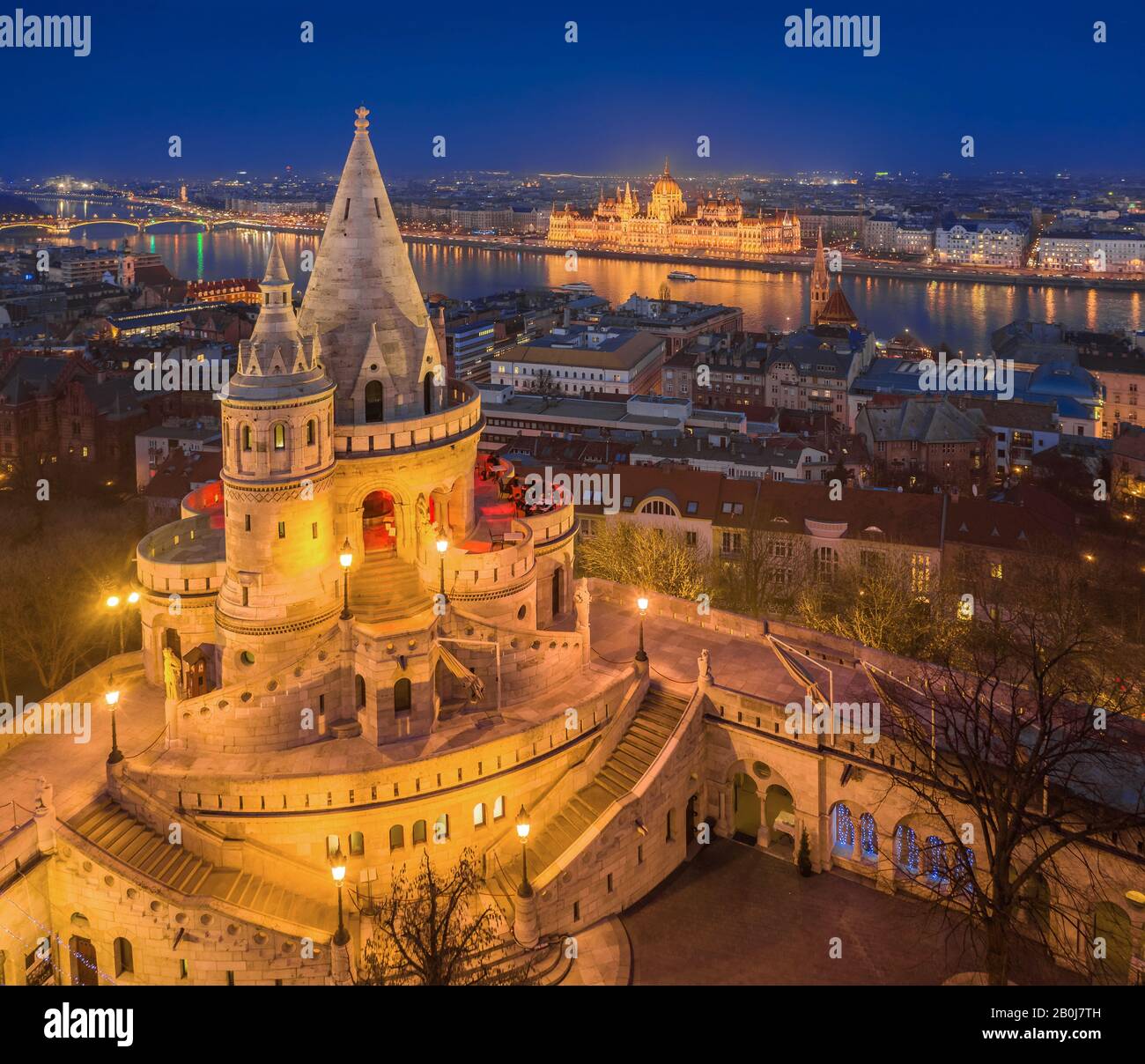 Budapest, Hongrie - vue aérienne de la tour principale de Fisherman's Bastion (Halaszbastya) avec Parlement éclairé de la Hongrie à l'heure bleue sur une trinte Banque D'Images