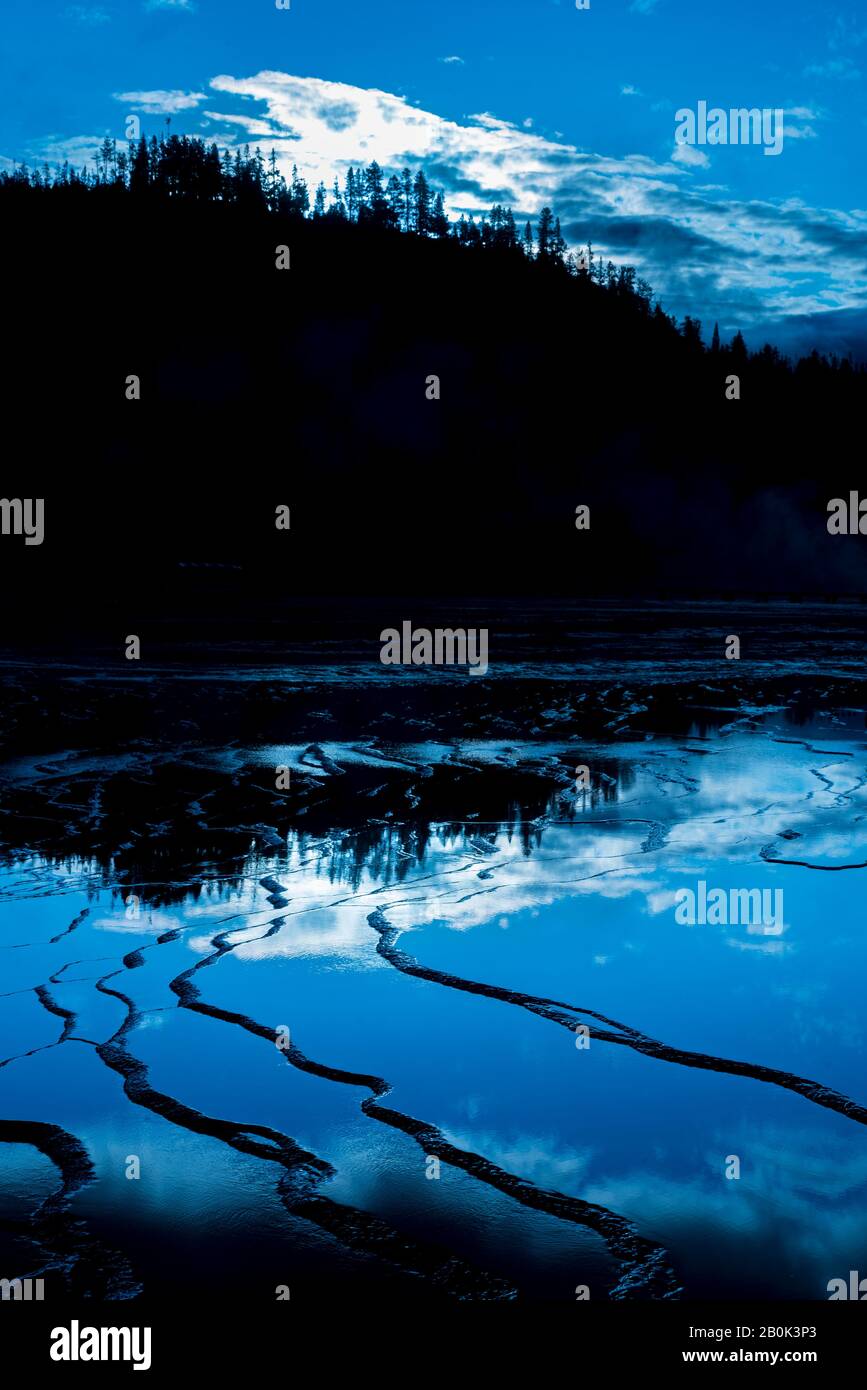 Miroir texturé comme la surface rocheuse reflétant les arbres et le ciel. Collines boisées sous un ciel bleu avec des nuages blancs. Banque D'Images