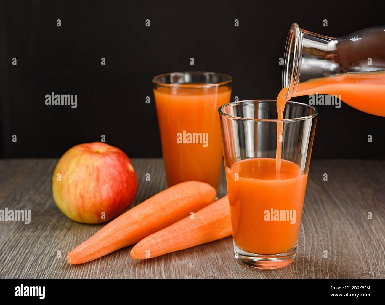 Le jus de pomme de carotte est versé de la bouteille dans un verre. Il y a des carottes et des pommes sur la table. Banque D'Images