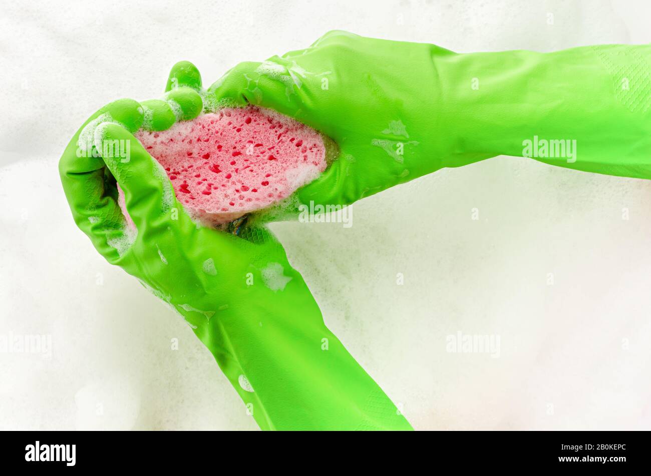 Main dans le gant de protection tenant une éponge savonneuse sur fond de mousse. Concept de lavage de vaisselle. Espace de copie Banque D'Images