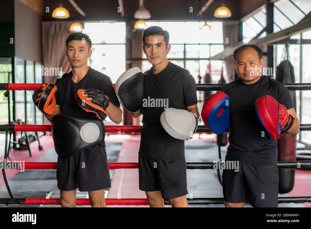 Trois boxeurs asiatiques regardant l'appareil photo et poser et sourire tout en se pencha sur des cordes rouges noires sur l'anneau de boxe, et ont un repos après une formation dure dans le bac Banque D'Images