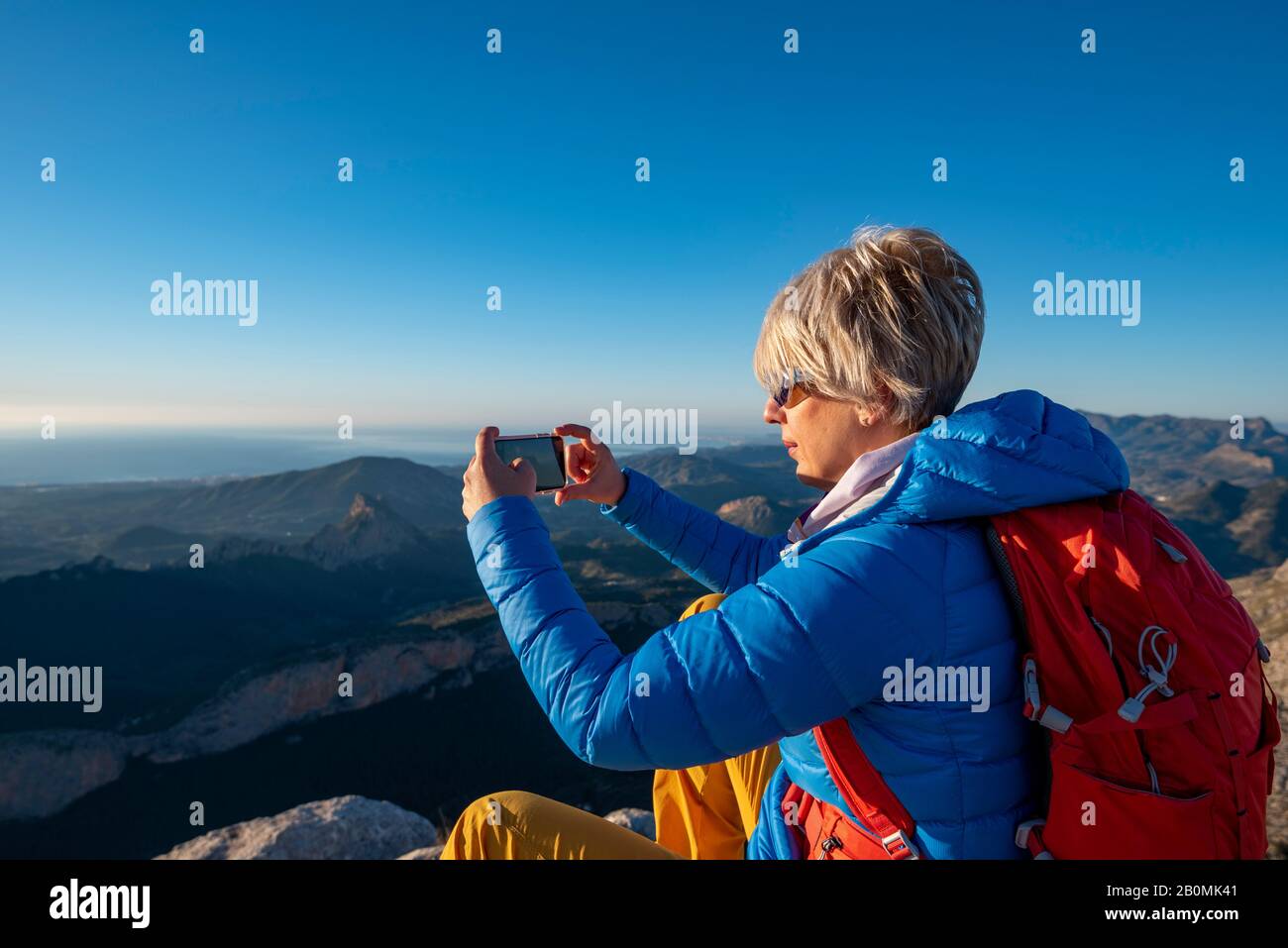 Jeune femme debout sur des rochers au sommet d'une montagne avec un téléphone portable. Banque D'Images